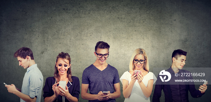 young people in casual clothes using mobile phone standing together against concrete wall