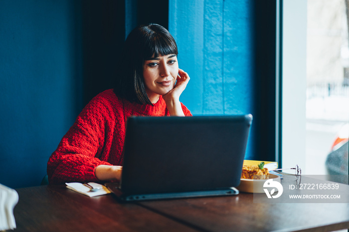 Carefree hipster girl enjoying shopping online via laptop computer during lunch at cafeteria, succes