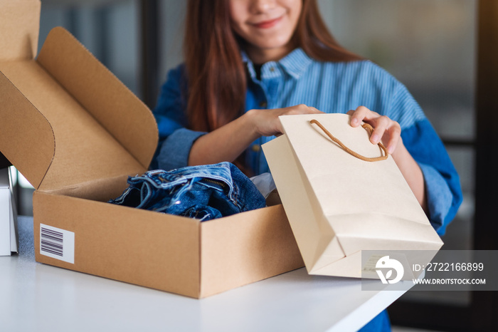 Closeup image of a woman opening and looking inside shopping bag with postal parcel box of clothing 