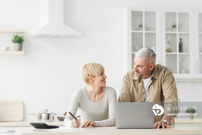 Smiling senior couple spouses use laptop, calculator, new technology paying banking bills online