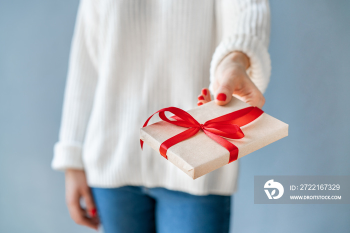 Close up cropped shot of woman hands with red polished nails holding gift box with red satin ribbon 