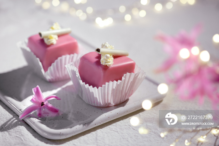 Valentine petit fours with marzipan icing. Fragrant pink hyacinth flower. Garland of lights on white