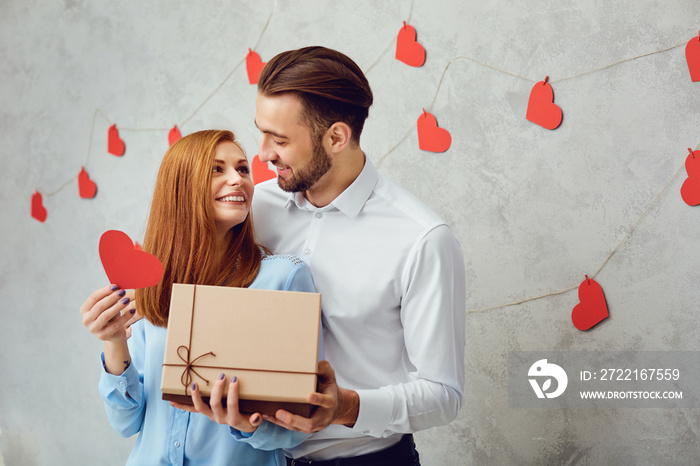 A young couple gives a gift on a gray background.