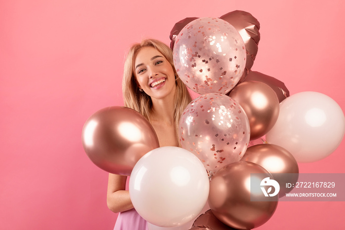 Charming millennial woman with bunch of air balloons having holiday party over pink studio backgroun