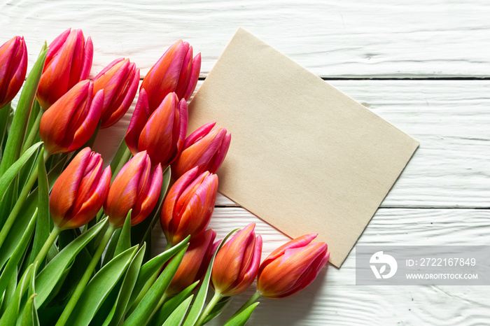 A bouquet of tulips and a piece of paper for text on a wooden background.