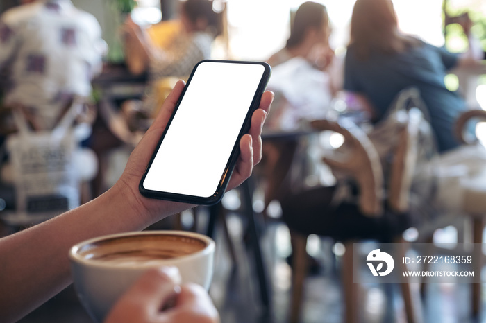 Mockup image of hands holding white mobile phone with blank screen while drinking coffee in modern c