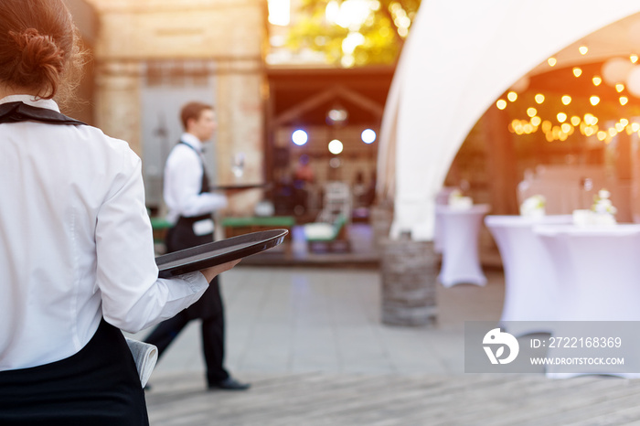 Waiter holding an empty tray in outdoor cafe. Catering service.