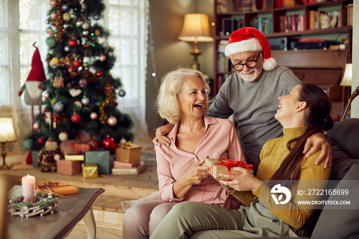 Young woman has fun while receiving Christmas present from her senior parents at home.