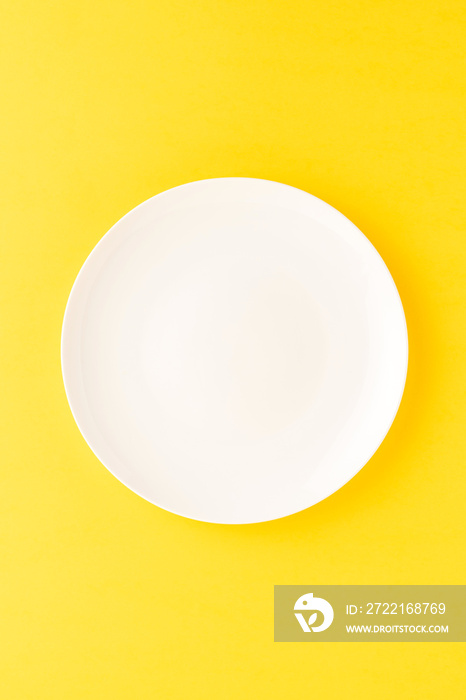 Empty white plate on yellow table. Top view