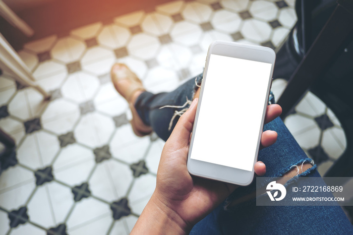 Mockup image of hand holding white mobile phone with blank white screen on thigh with a vintage tile