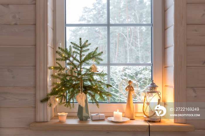 Christmas lantern, Christmas Angel, Christmas tree and white decor on the window of a wooden house