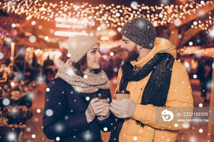 Close up photo of beautiful young couple outdoors at winter snowfall on a new year`s eve with hot dr