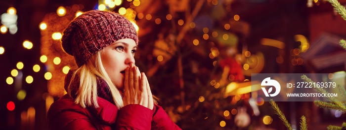 Outdoor photo of young beautiful happy smiling girl posing in street. Festive Christmas fair on back