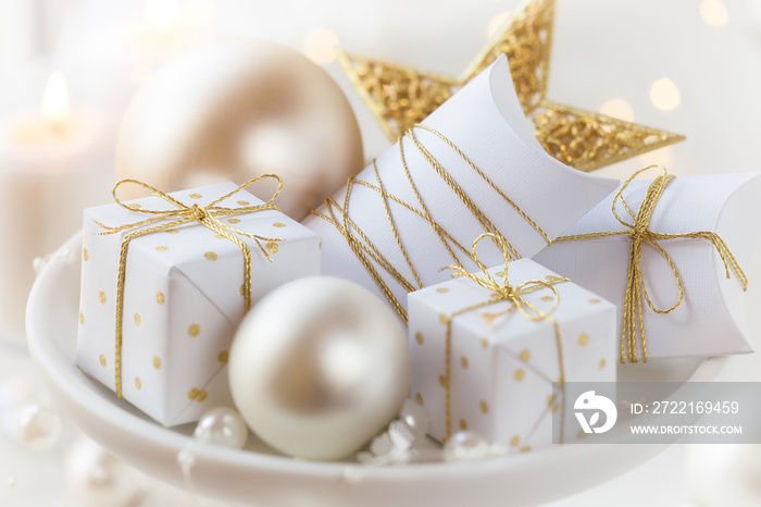 White Christmas gifts with golden ribbons on a stand with festive Xmas decorations and baubles