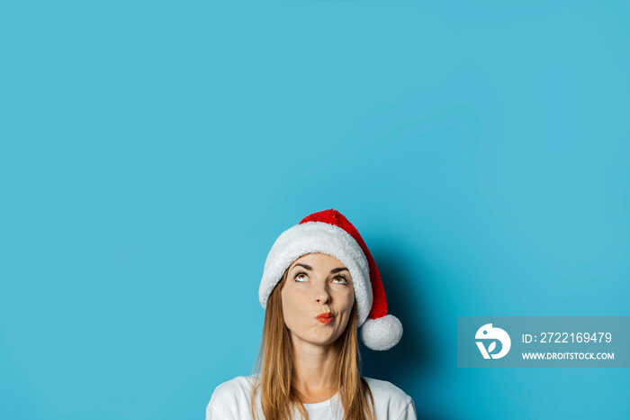 Young woman in Santa Claus hat with a mysterious face on a blue background. Concept idea for new yea