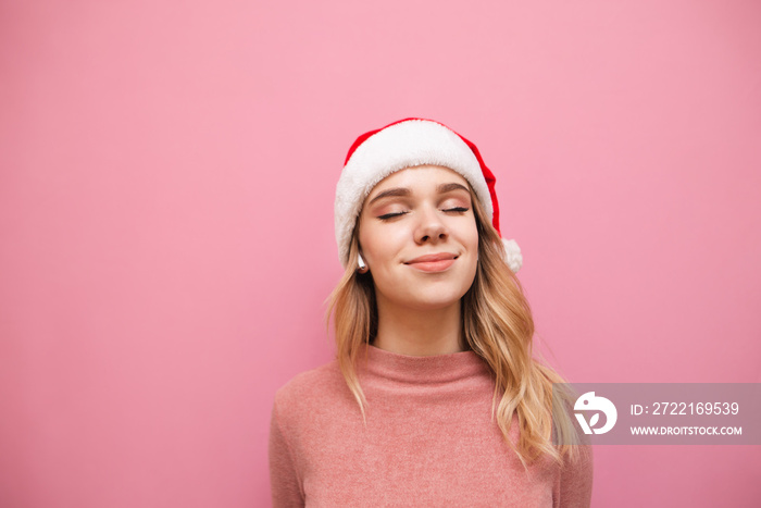 Satisfied attractive blonde girl in santa hat listening to music in closed-loop wireless headphones 