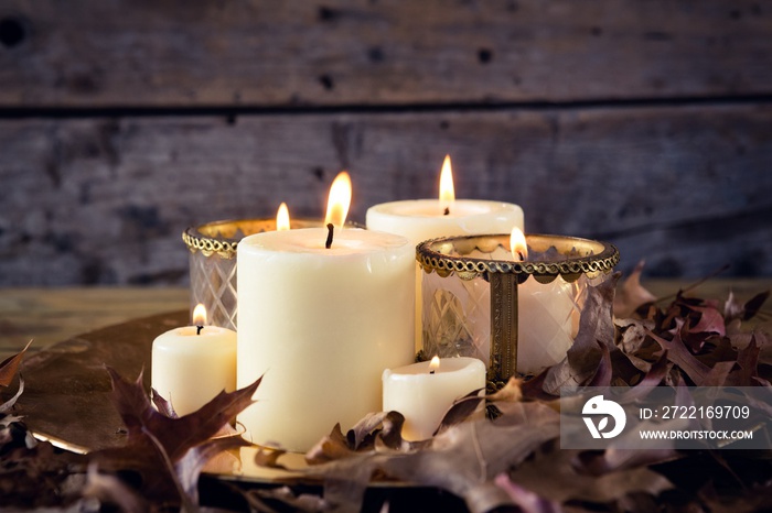 Lit candles and dry leaves on table