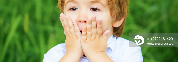 Funny child boy with hands close to face isolated on green background. Child expressing surprise with his hands in his face. Smiling amazed or surprised child boy. Shocked and surprised boy