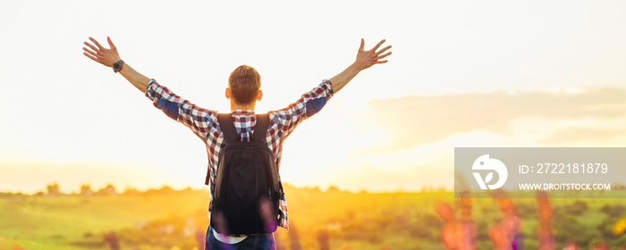 Traveler with raised hands standing on a hill in green grass and enjoying a majestic sunset, Successful man enjoying triumph