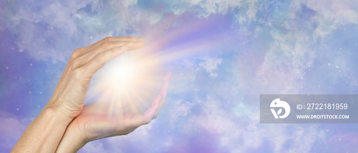 Sending Beautiful Healing Light across distance  - female hands cupped around a bright burst of light against a celestial cosmic sky  background with copy space