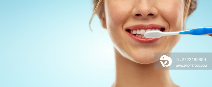 oral care, dental hygiene and people concept - close up of smiling woman with toothbrush cleaning teeth over blue background