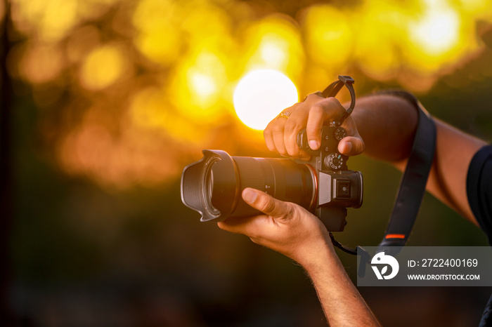 Closeup of a black camera holding by Photographer’s hand with sunset background