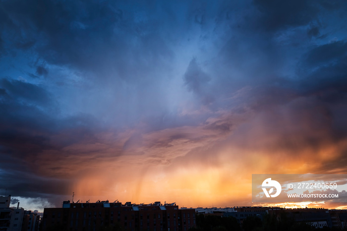 a summer storm at sunset over a city with a sky in shades of orange and blue, contrasting bluish and orange complementary colors in a dramatic sky