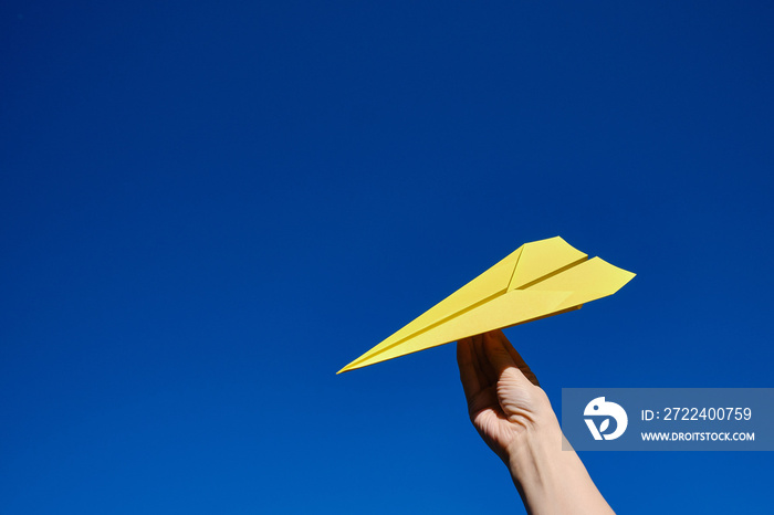 Paper yellow plane in the hands against the blue sky. Taking flight! Travel concept