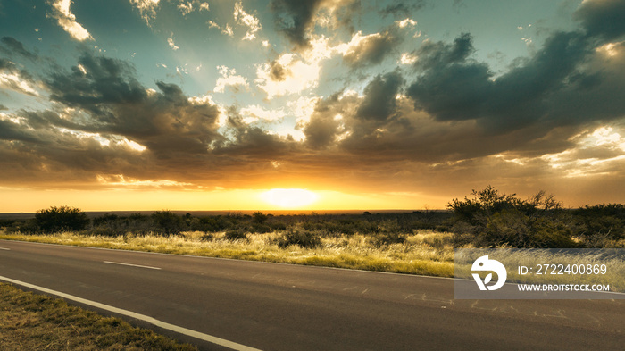 Panoramic sunset during golden hour with flat landscape, cloudy sky and road in the foreground