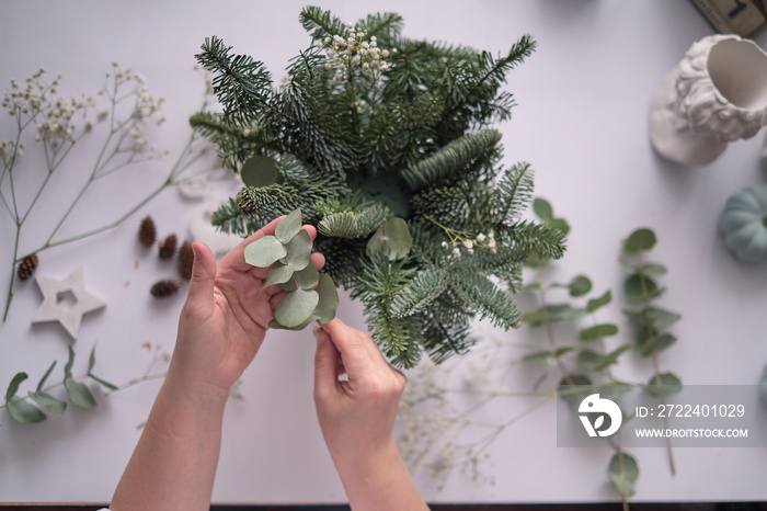 Woman decorated a Christmas table decoration. Hands close-up. Master class on making decorative ornaments. Christmas decor with their own hands. Flower shop. Christmas composition of fir branches.