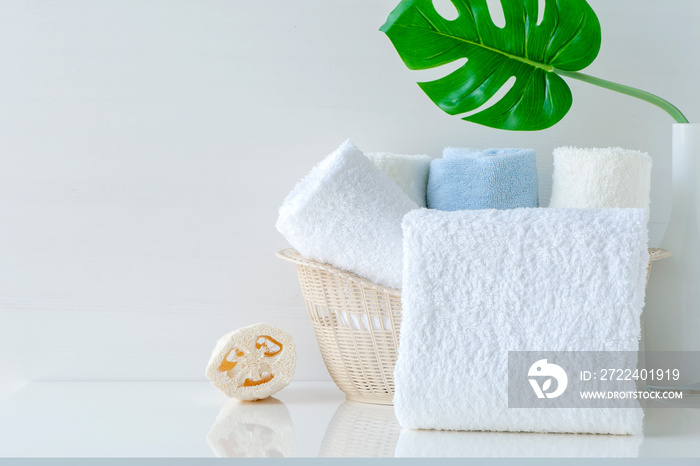 Clean bath towels in basket and houseplant on white table.