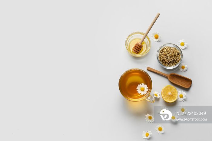 Composition with tasty chamomile tea, flowers and honey on grey background