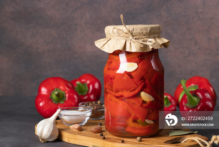 Pickled sweet peppers with garlic in glass jar on brown background