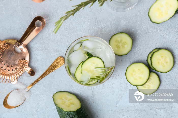 Glass of cold gin tonic and cucumber slices on light background