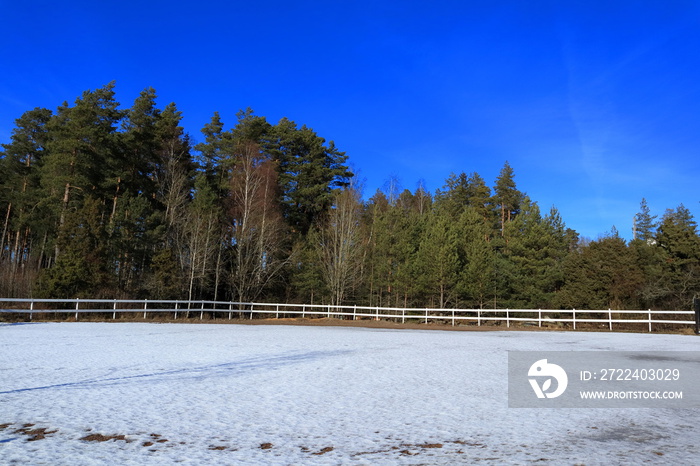 Snow covered ground at a stable. Still winter, soon spring. Nice weather outside. Fence and green forest. Sigtuna, Stockholm, Sweden, Europe.