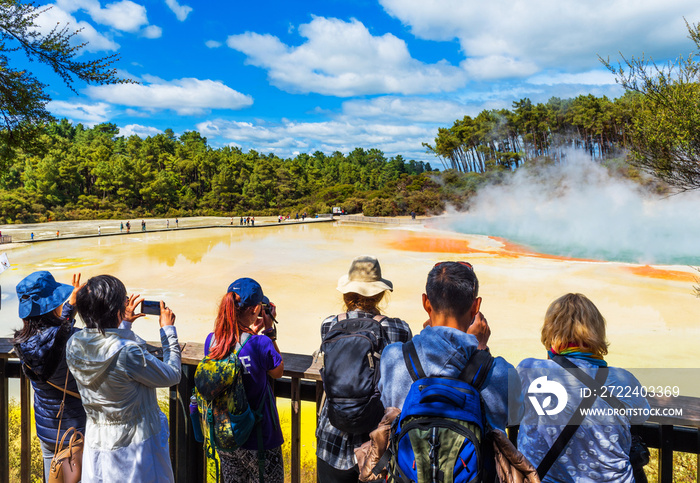 A group of people on the background of geothermal pools in Wai-O-Tapu park, Rotorua, New Zealand.