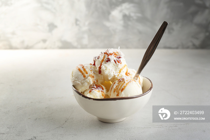 Bowl with balls of coconut ice cream and caramel syrup on light background