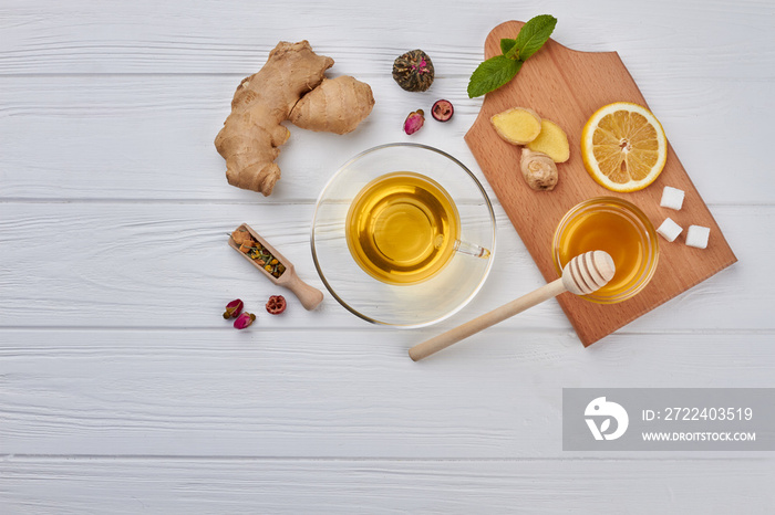 Cup of tea, lemon and ginger on wooden background. Fresh ginger root, cup of tea, lemon slice, honey and green plant. Ingredients for healthy beverage.