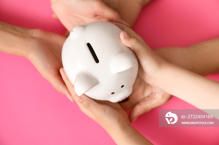 Hands of family with piggy bank on color background