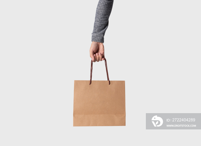 Hand holding blank brown paper bag for mockup template advertising and branding on gray background.