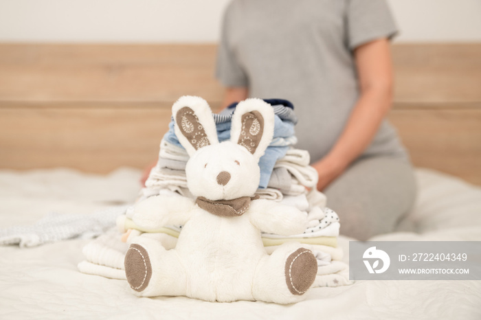 Pile of baby clothes, rabbit and pregnant woman on a bed