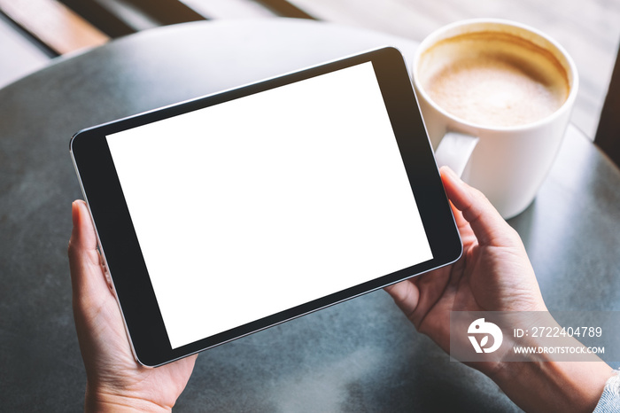 Mockup image of a woman holding black tablet with white blank screen and coffee cup on the table