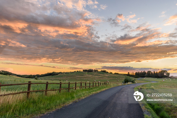 Landschaft in der Toskana mit Hügeln, Häusern , Zaun, und Straße bei Sonnenuntergang