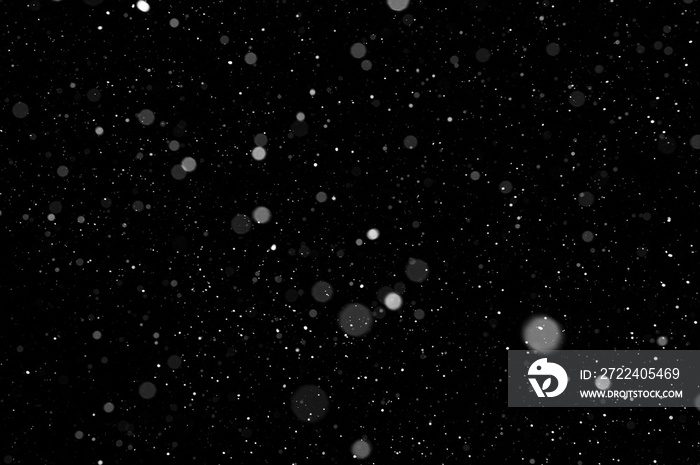 Bokeh of white snow on a black background. Falling snowflakes on night sky background, isolated for post production and overlay in graphic editor.