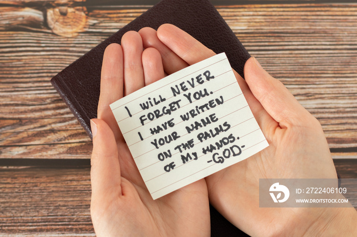 Woman hands palms holding a handwritten note with Bible quote on wooden background. Christian biblical concept of God Jesus Christ love, mercy, and grace for His people. Top view.