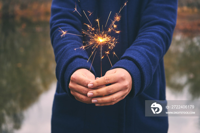 Woman holding sparkler in forest, winter day