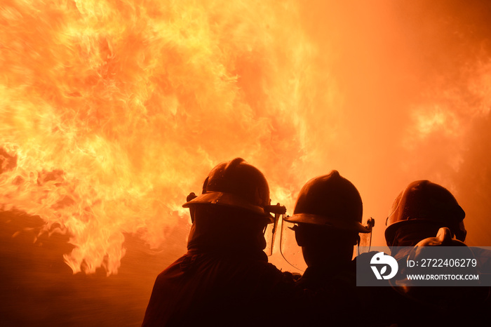 firefighters with fire hose fight with fire at night