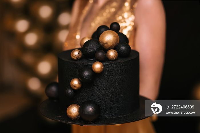 close-up of a girl holding a black cake with golden balls. Celebration concept, birthday.