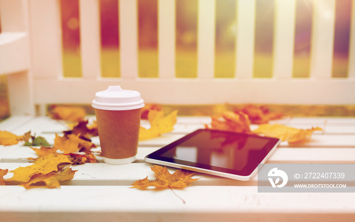 tablet pc and coffee cup on bench in autumn park