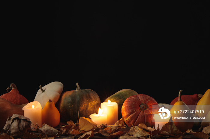 dry foliage, burning candles, ripe pumpkin on wooden rustic table isolated on black